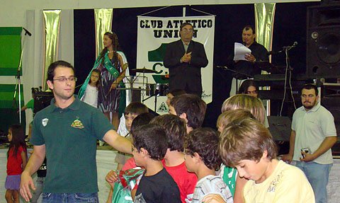 Adelante, los chicos pasan en el banderazo, mientras desde el escenario, el presidente del club, Jorge Rambaudo y la reina, Yamila Majluf, observan.